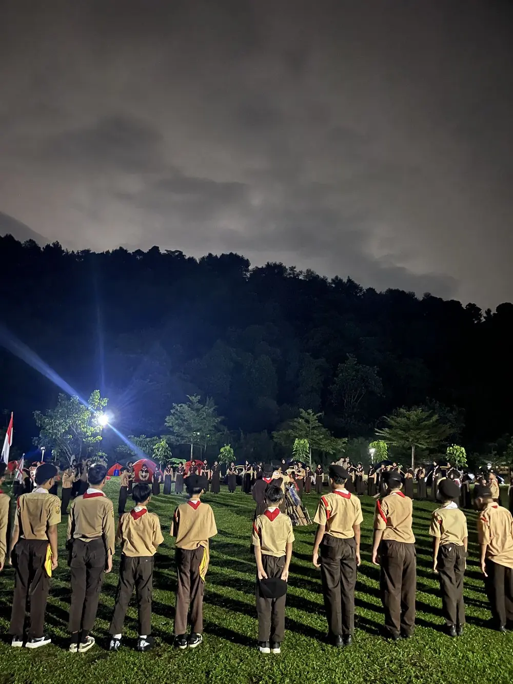 Barisan pramuka berdiri di lapangan rumput pada malam hari