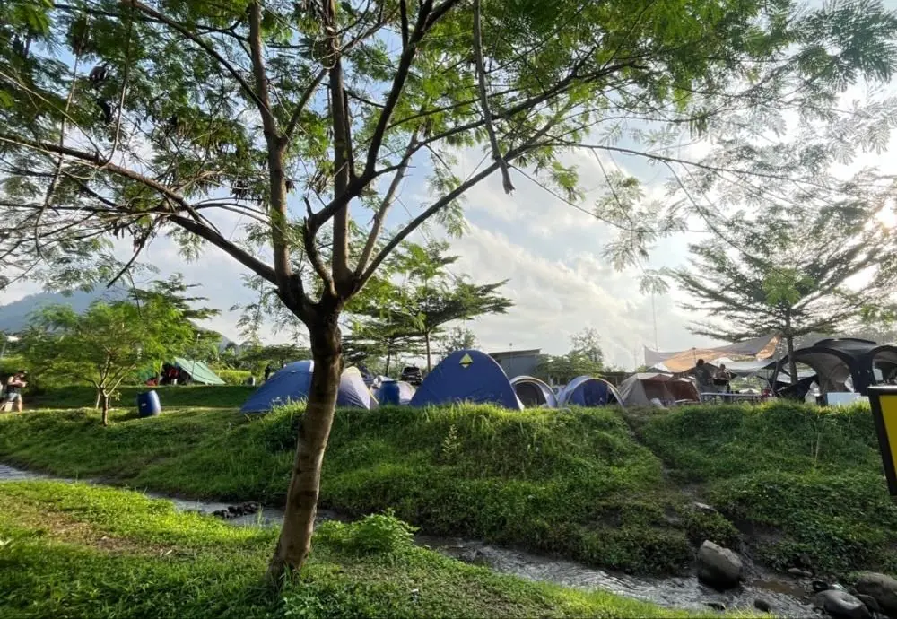 Aliran sungai kecil di depan deretan tenda di bawah pepohonan