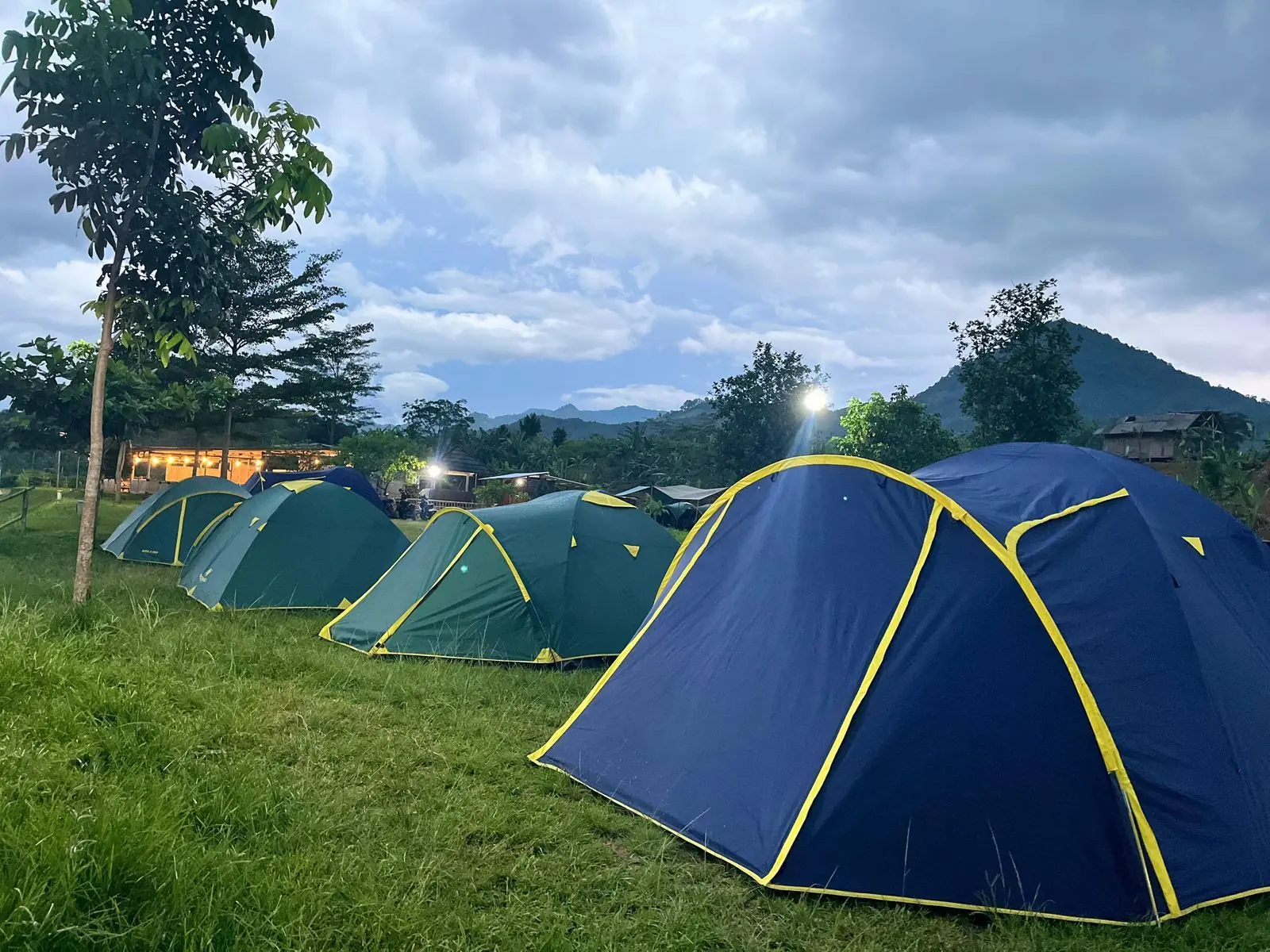 Tenda dome biru dan hijau di padang rumput Sisi Cai dengan latar perbukitan